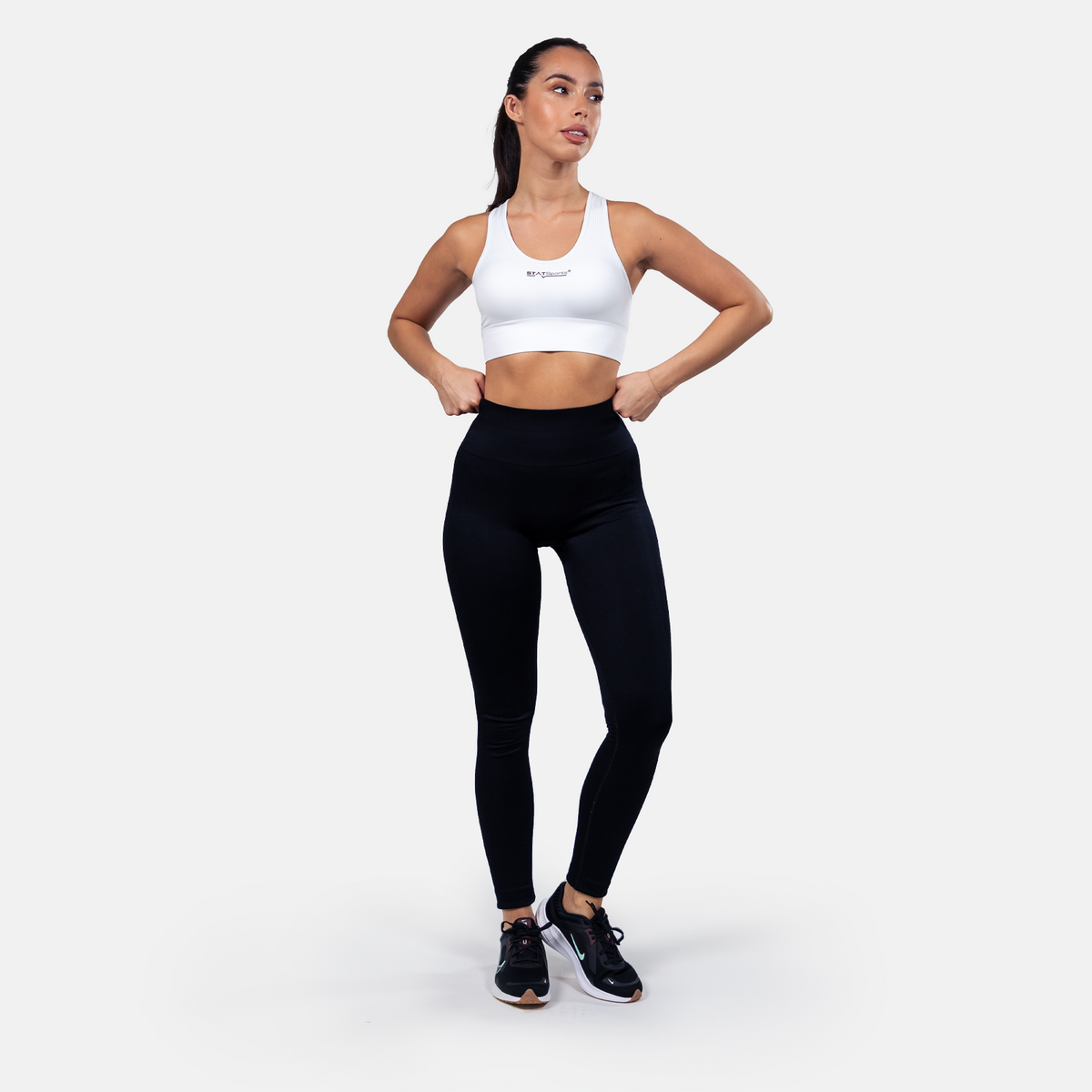 Woman wearing the white STATSports sports bra with leggings, full-length view