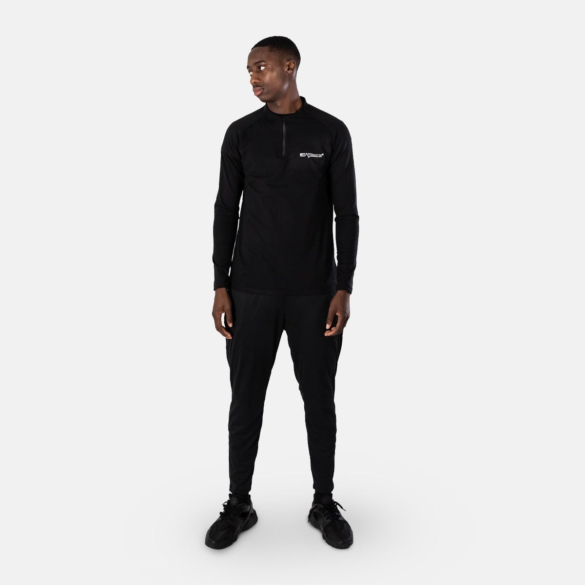 Man wearing the black STATSports Men's Performance Drill Top with matching trousers